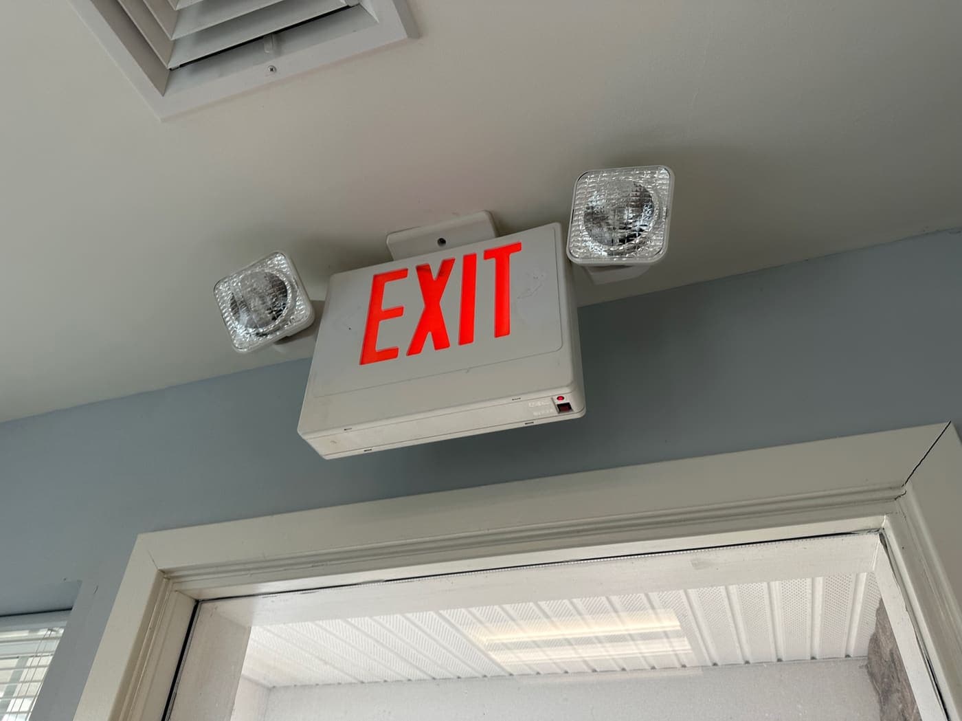 Combination exit sign and emergency light unit mounted above a doorway