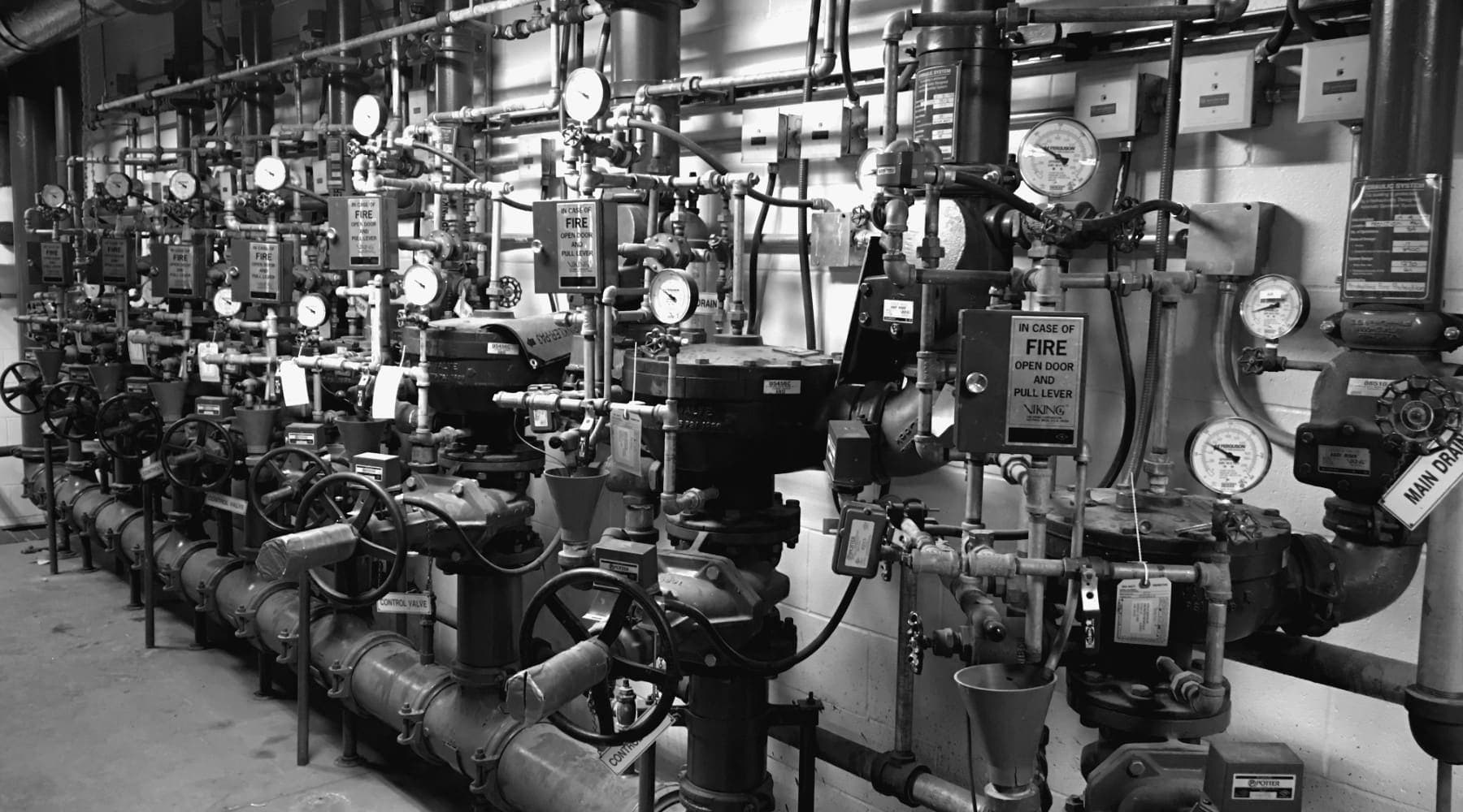 Wall of sprinkler risers and valves in a commercial building, each with its own inspection tag